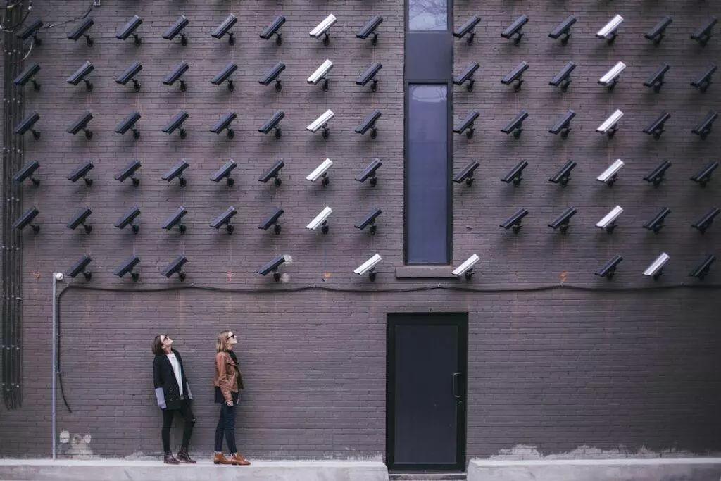 Two people standing in front of a wall with surveillance cameras.