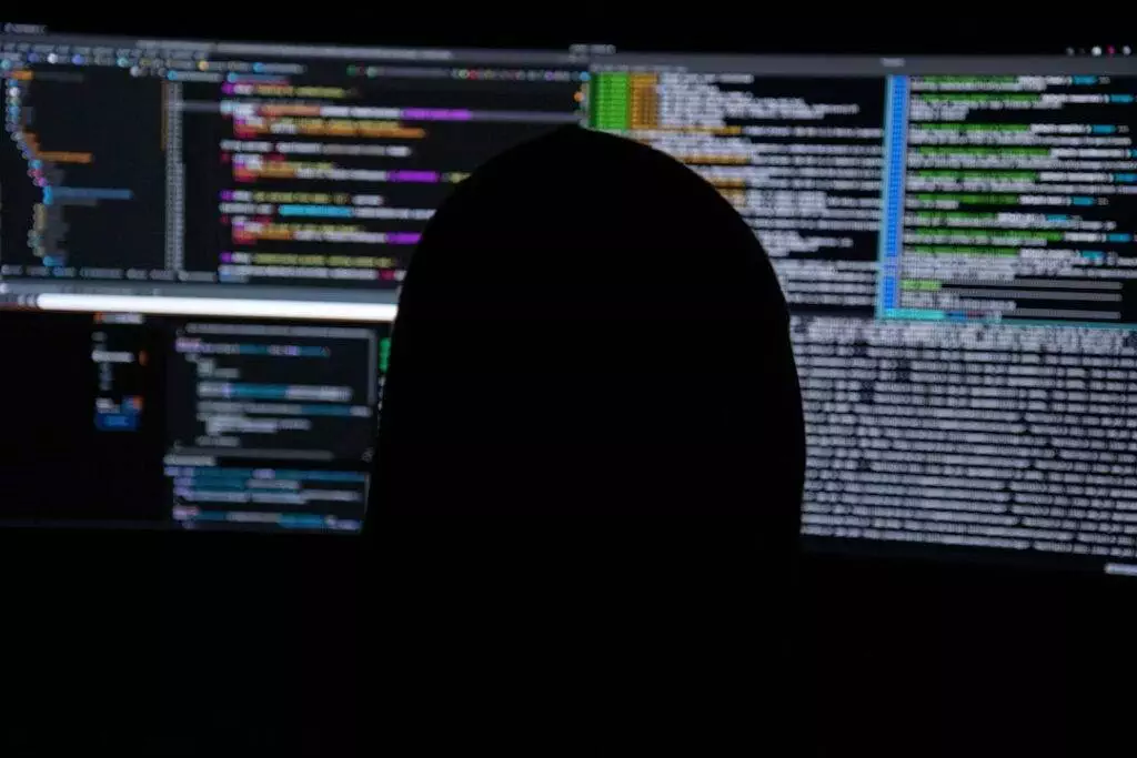A silhouette of a person sitting in front of a computer screen.